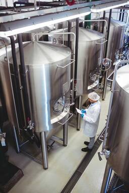 High angle view of manufacturer standing amidst storage tanks at brewery